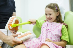 Girl in dentists chair toothbrushing a model